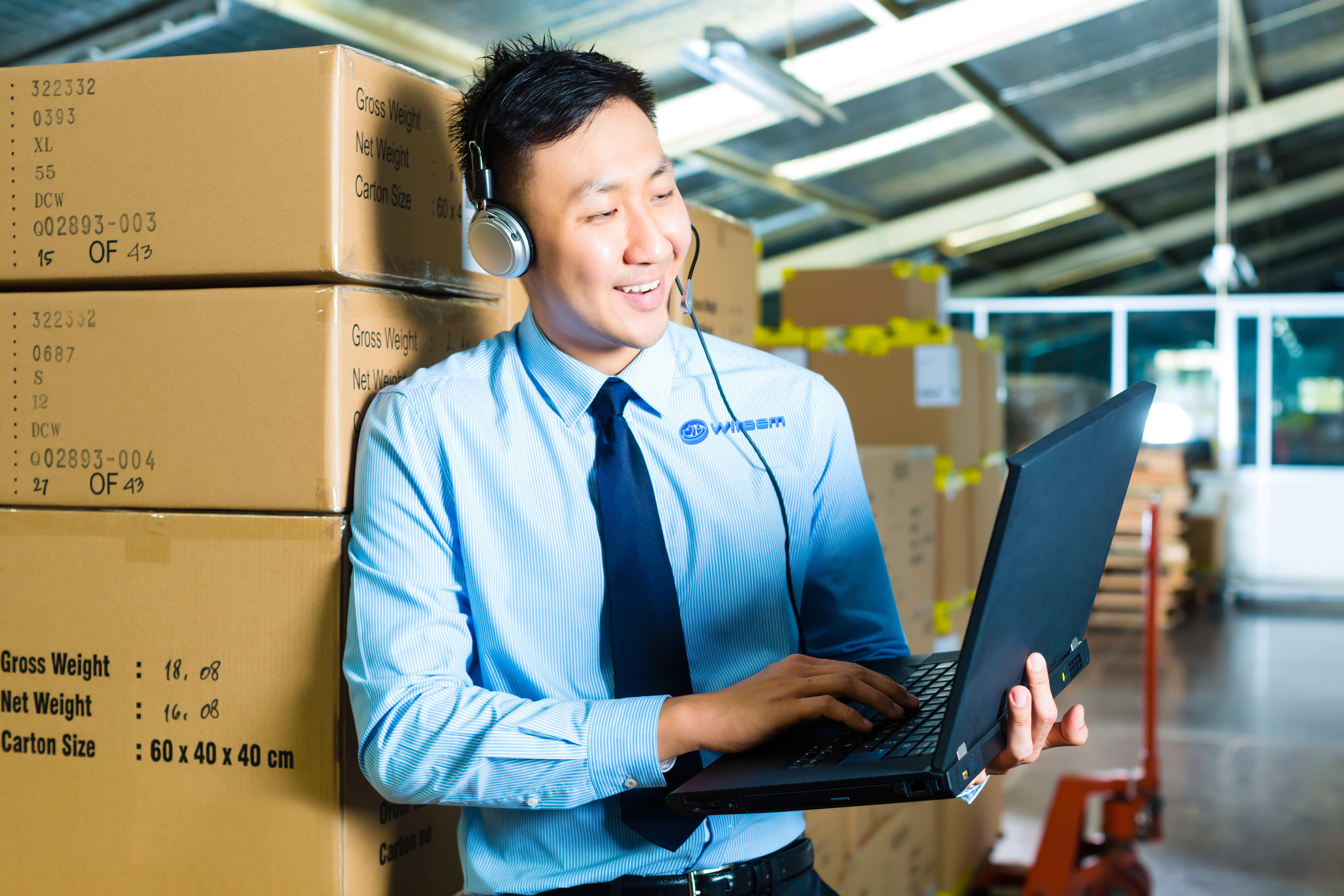 Young man in a suit with headset and laptop in a warehouse, he is from the Customer Service